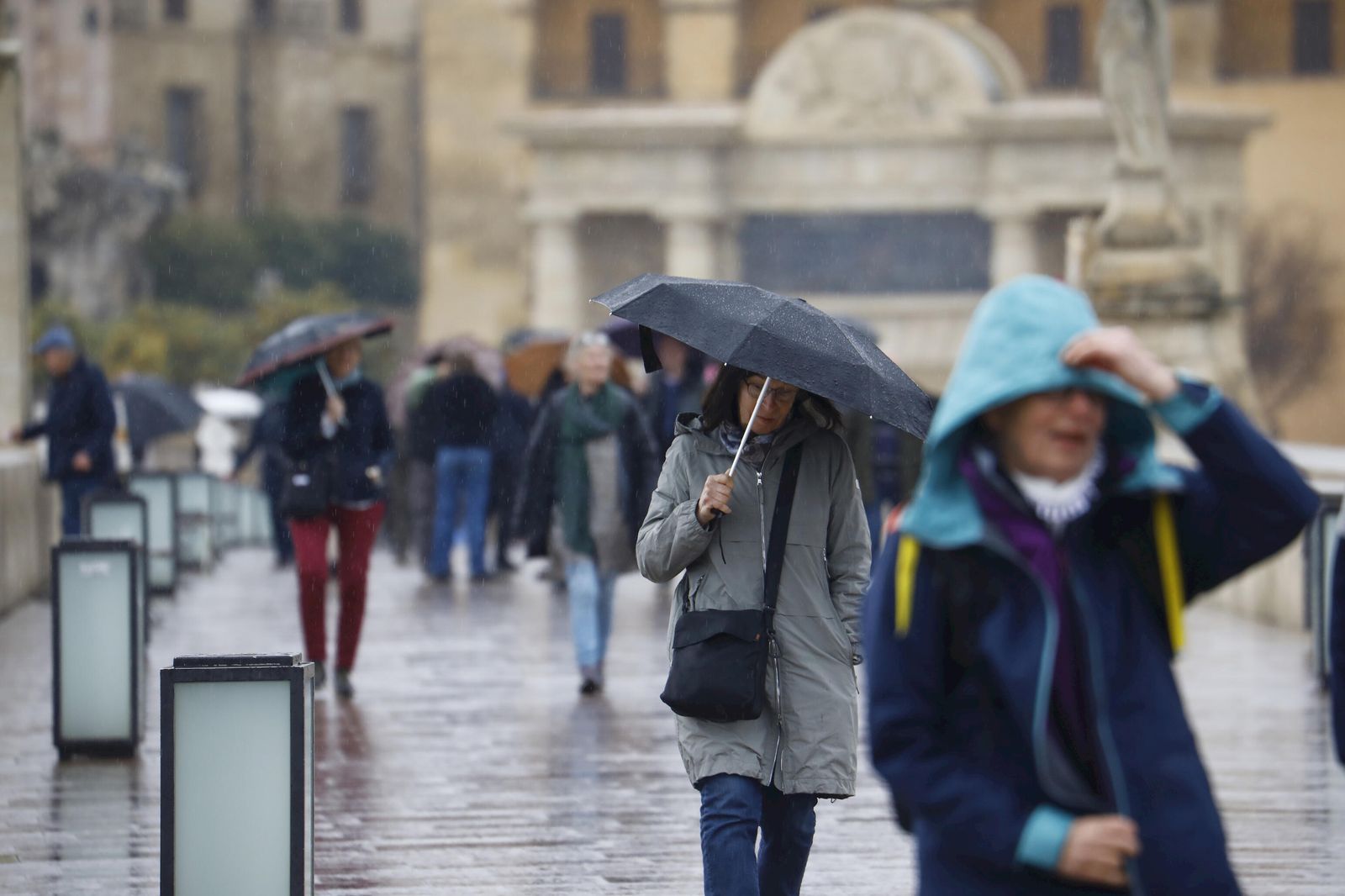 Varias personas se protegen de la lluvia  con paraguas mientras pasean por el puente Romano de Córdoba.