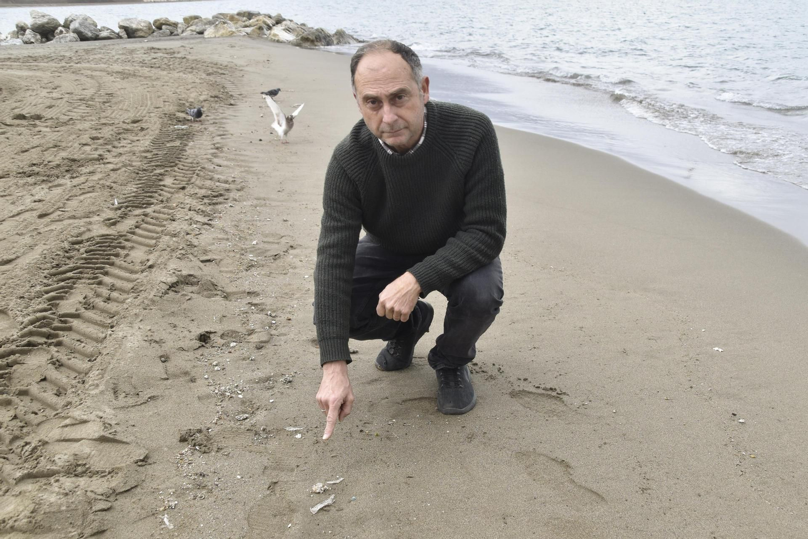 El biólogo y profesor del Instituto Universitario de Biotecnología y Desarrollo Azul (IBYDA) de la Universidad de Málaga (UMA) Juan Jesús Martín, posa en una playa de Málaga junto a pequeños residuos plásticos en la orilla.