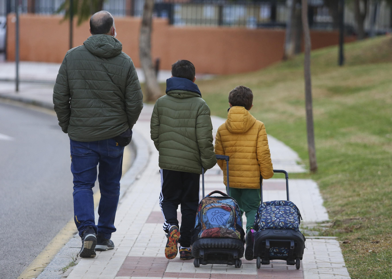 Un padre llevando a sus dos hijos al colegio.