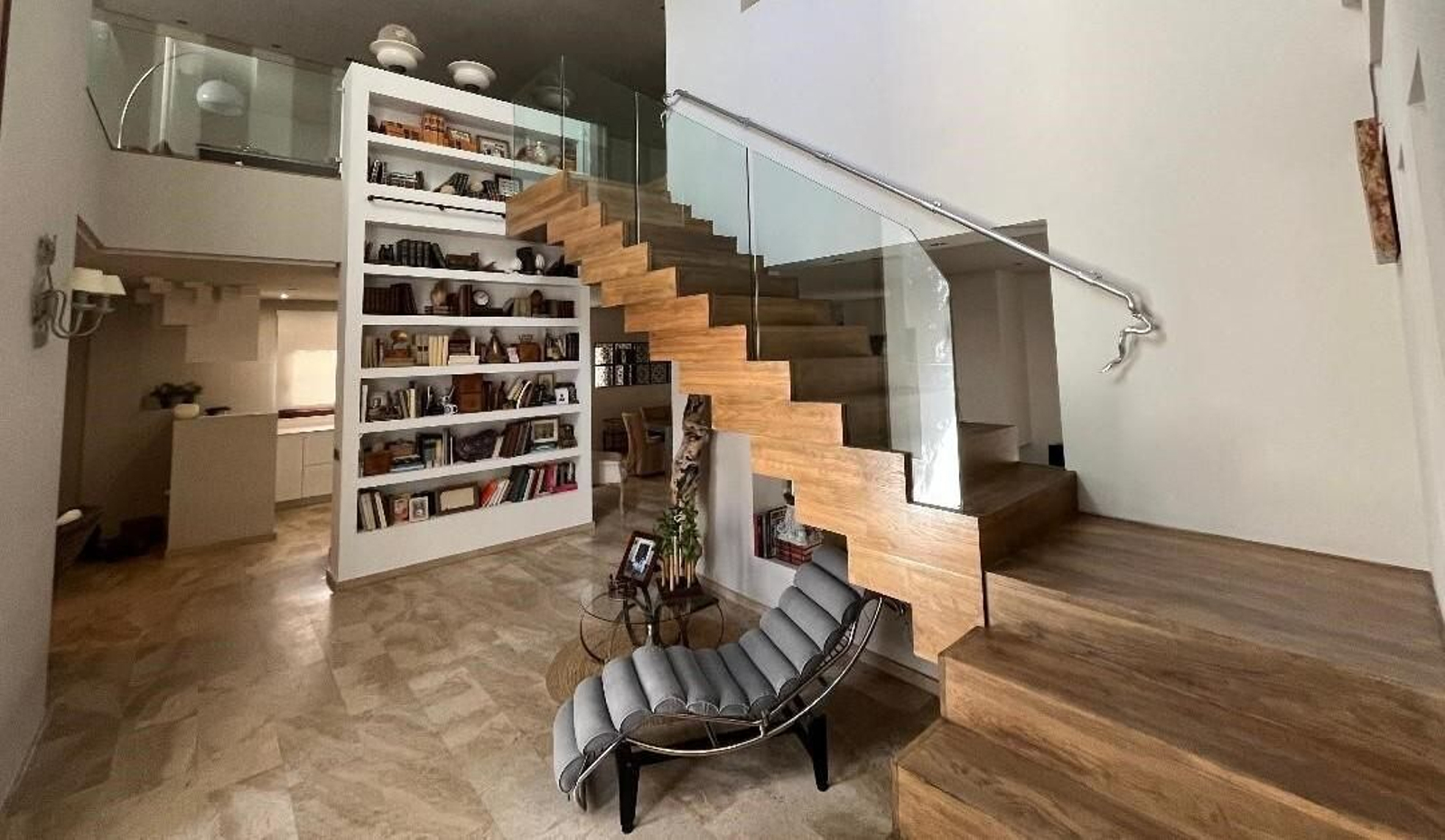 El hall lo ocupan una gran biblioteca y un   diván junto con unas escaleras que comunican con la planta superior.