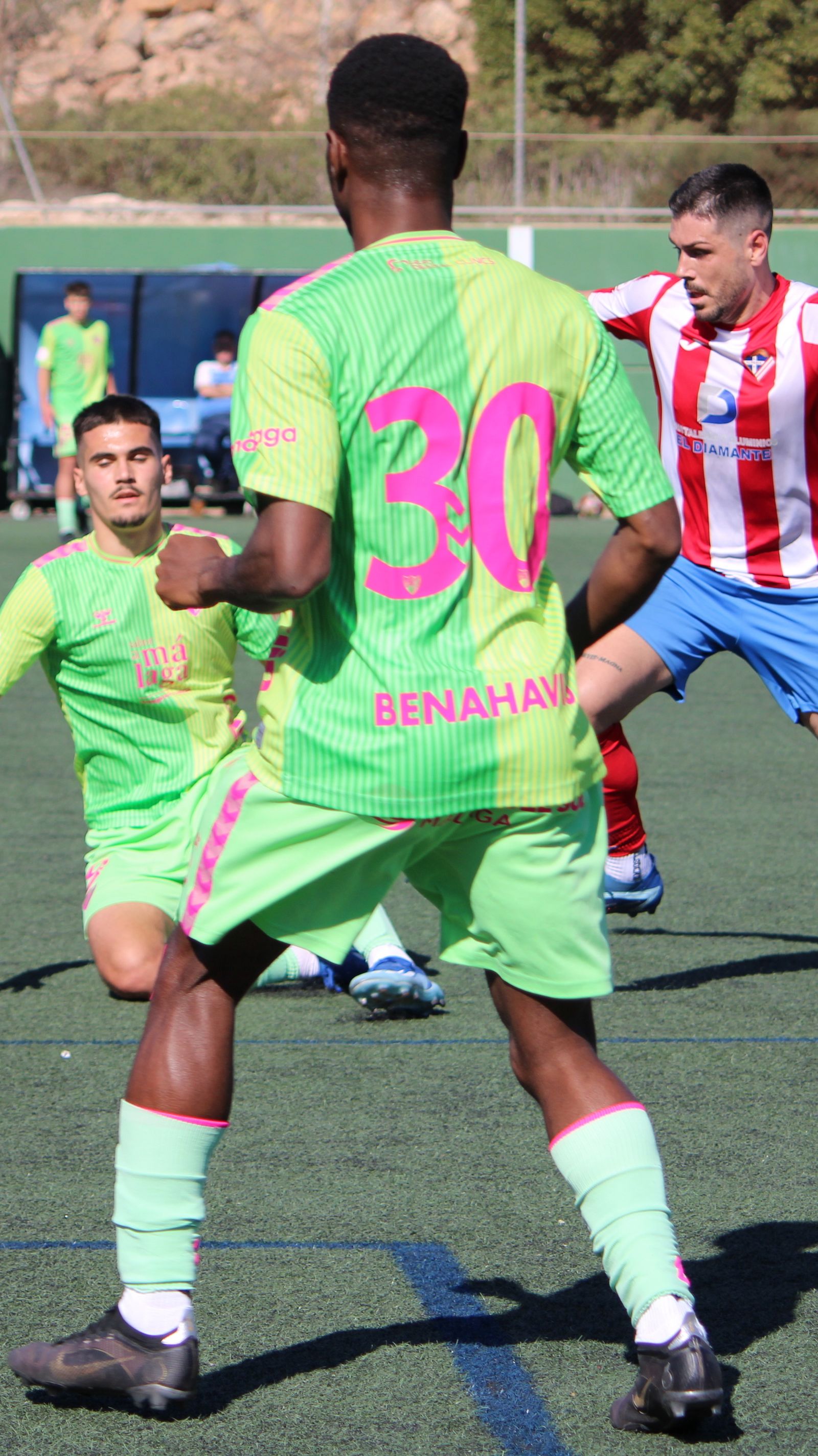 Un jugador local trata de irse de un futbolista del filial malagueño.