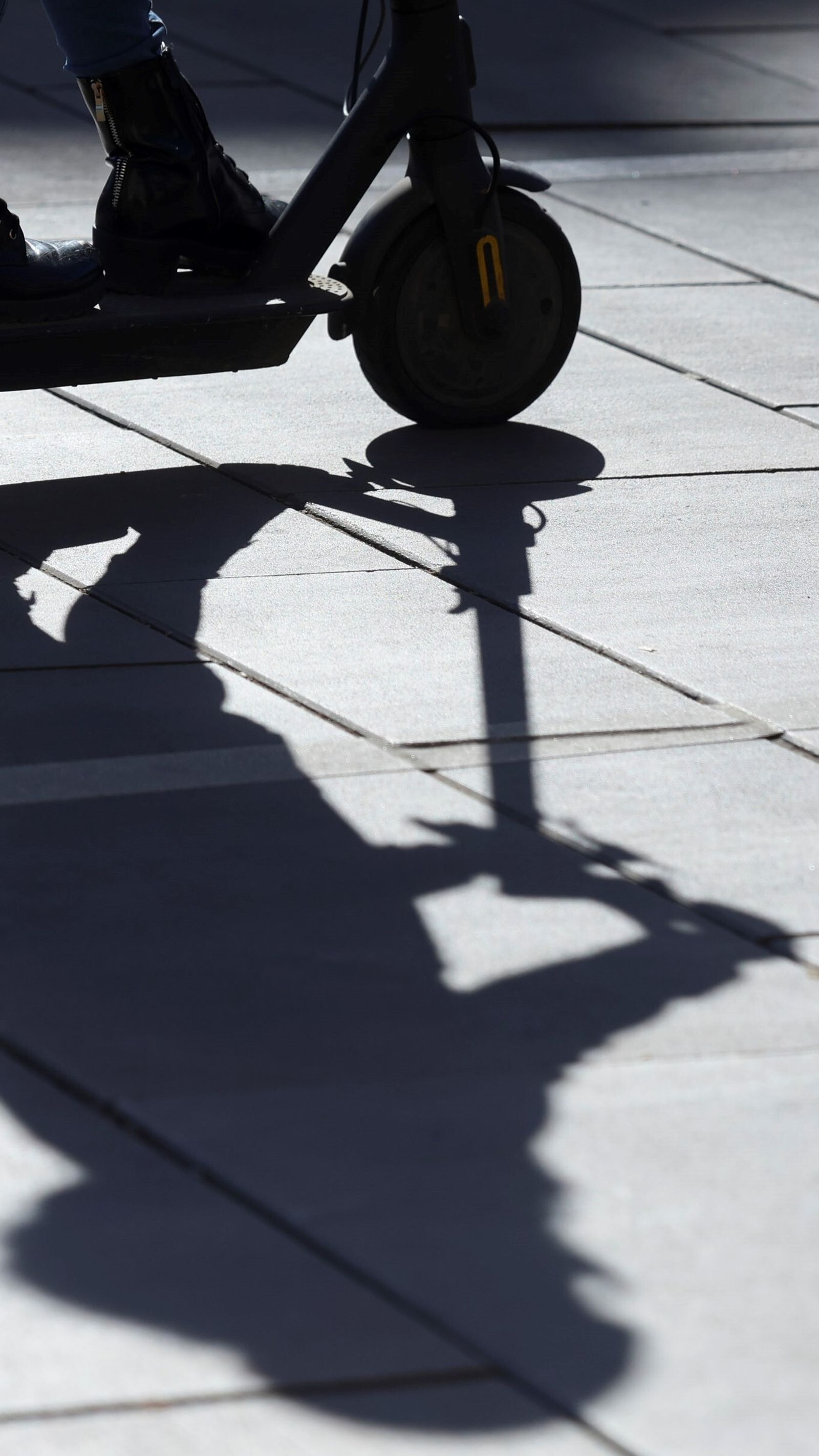 La sombra de un conductor de patinete proyectada en el pavimento.