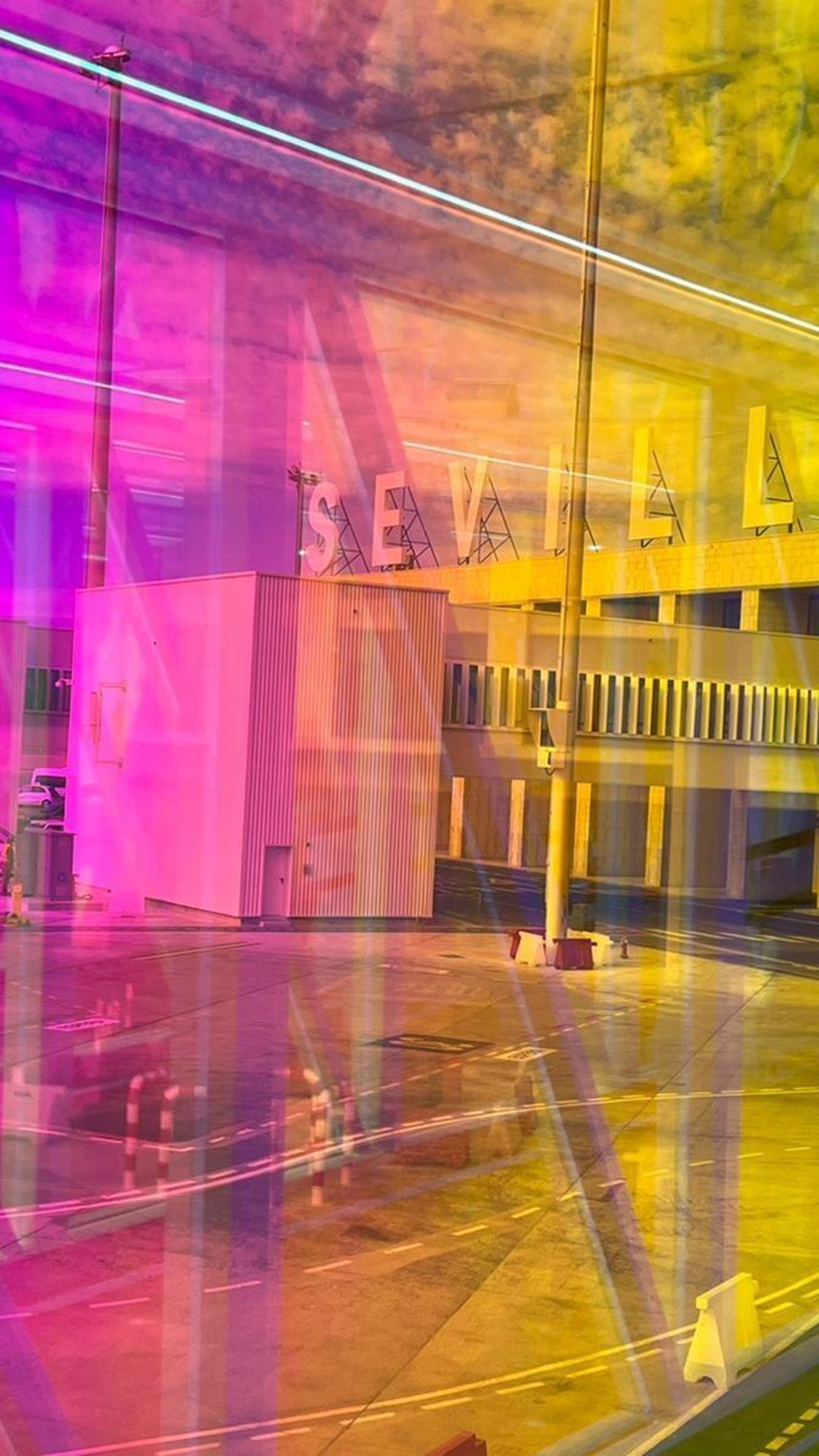 Pasarela de colores del aeropuerto de Sevilla con el letrero de Sevilla al fondo.