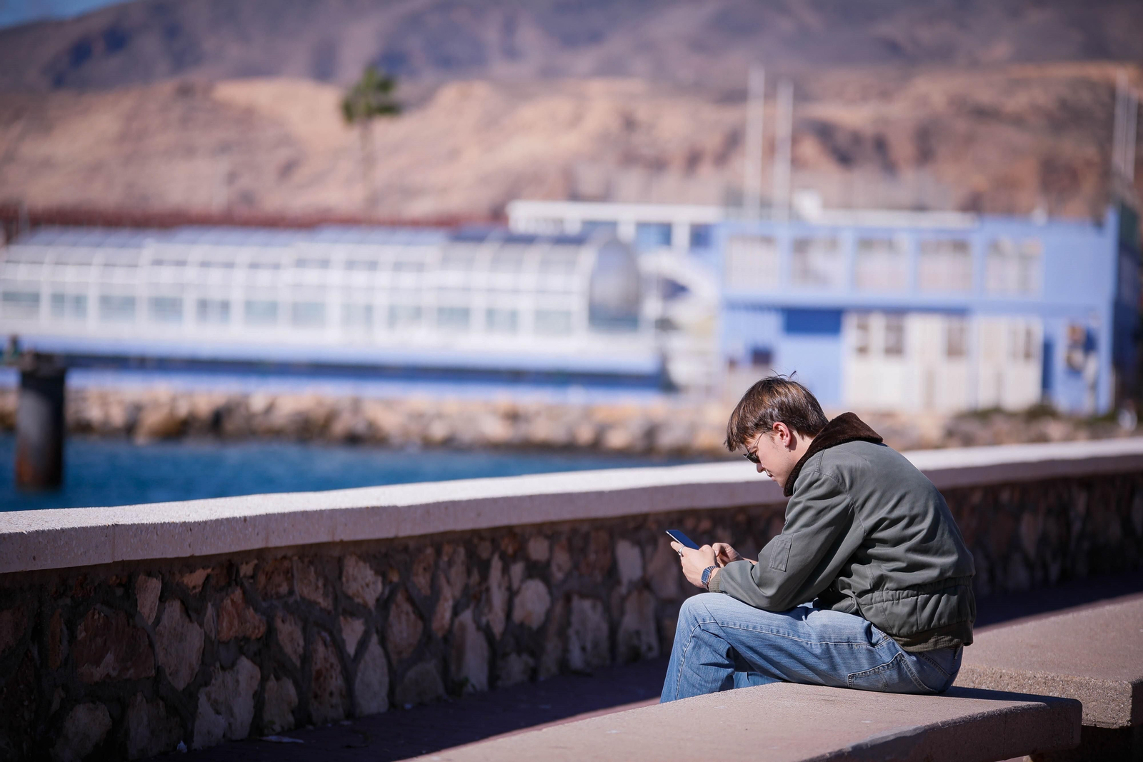 Un joven usa su teléfono móvil sentado en un banco del Paseo Marítimo de la capital almeriense.