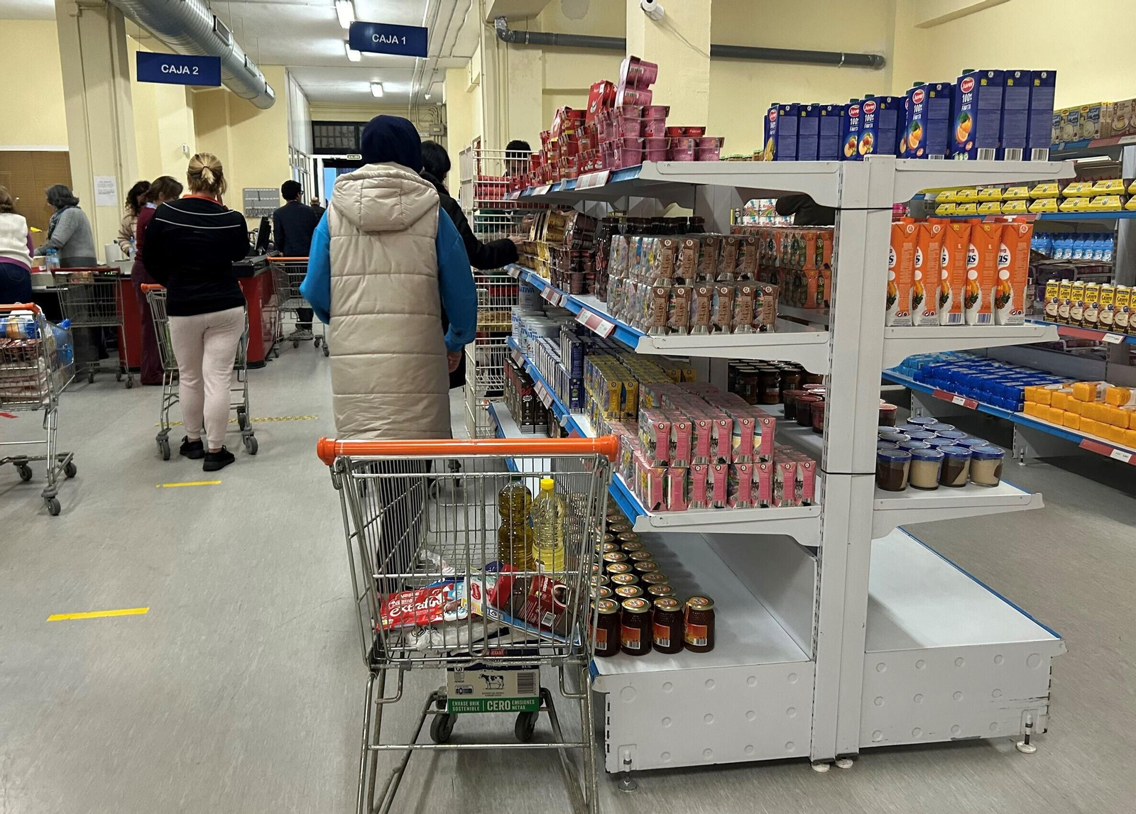 Panorámica del interior del economato donde unos compran y otros hacen colas para pagar.