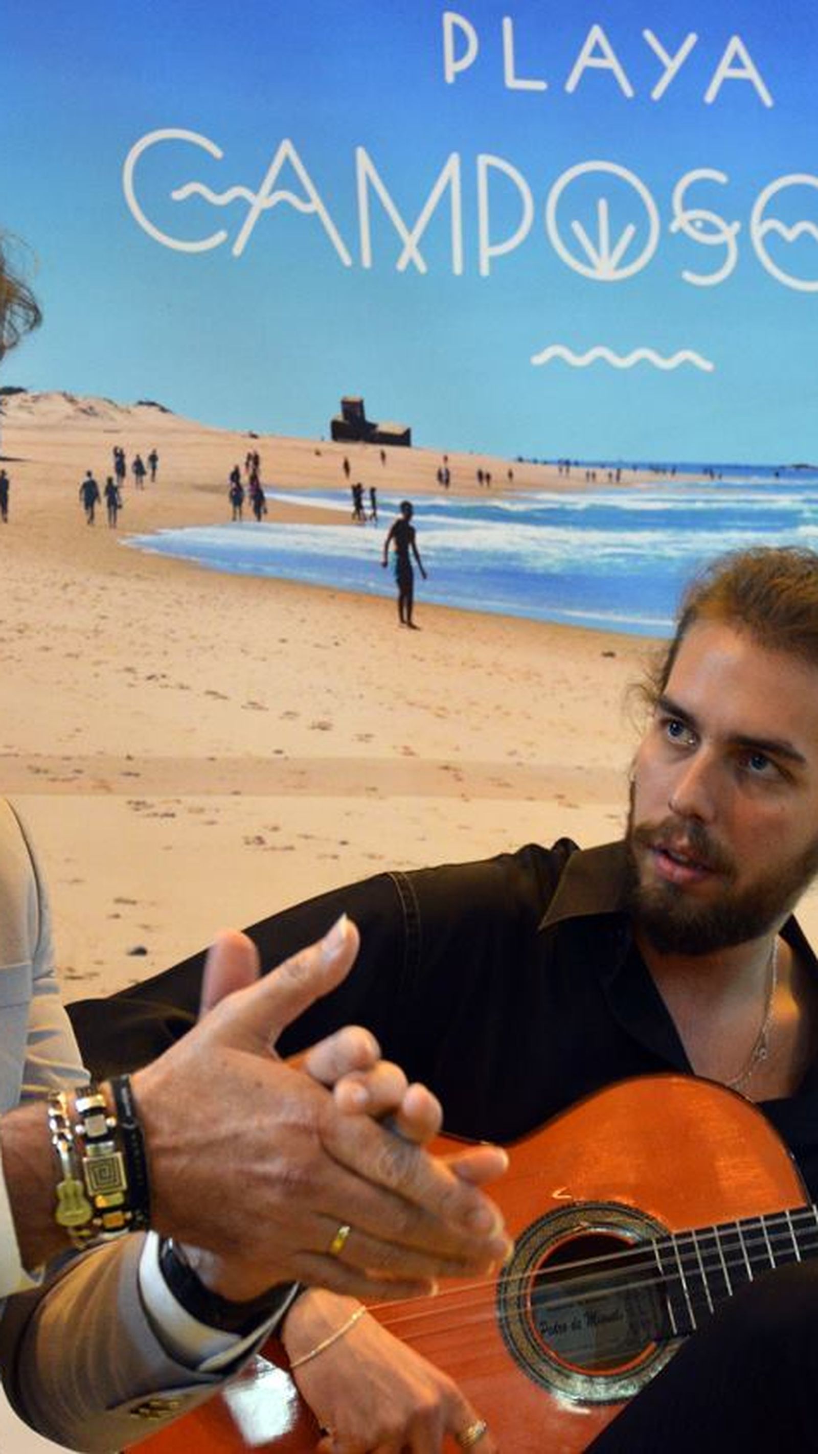 El cantaor Jesús Castilla actuando en una presentación del Ayuntamiento de San Fernando en FITUR. En el fondo, una imagen promocional de la playa de Camposoto.