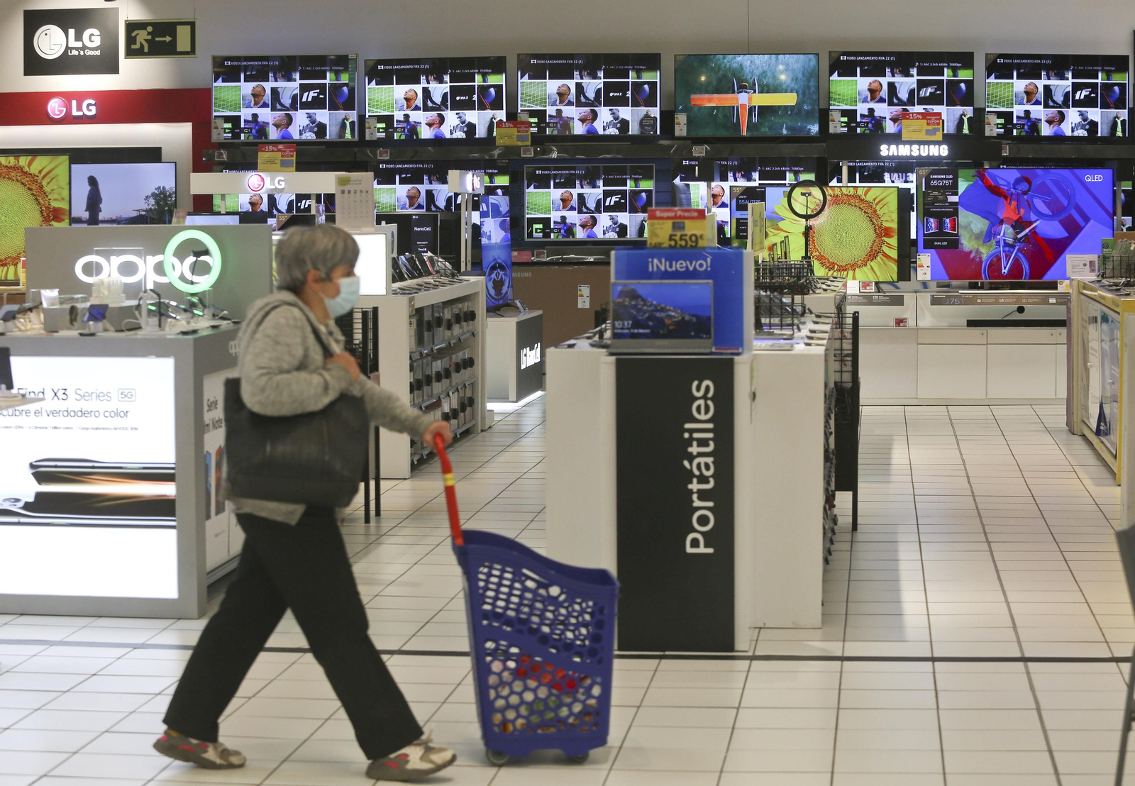 Mujer pasando por el pasillo de las televisiones en un supermercado.