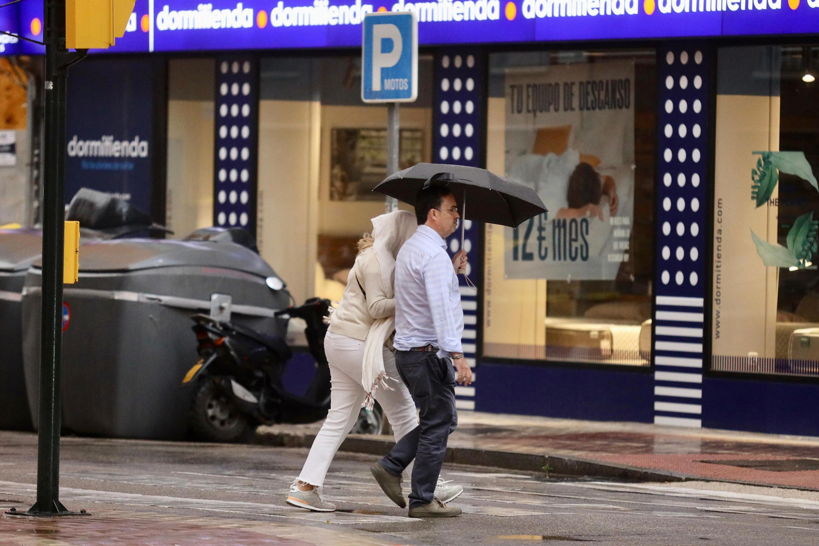 Una pareja se protege de la lluvia con un paraguas en una céntrica calle de Málaga